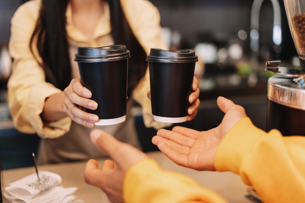 Barista giving takeaway coffee to customer in cafe